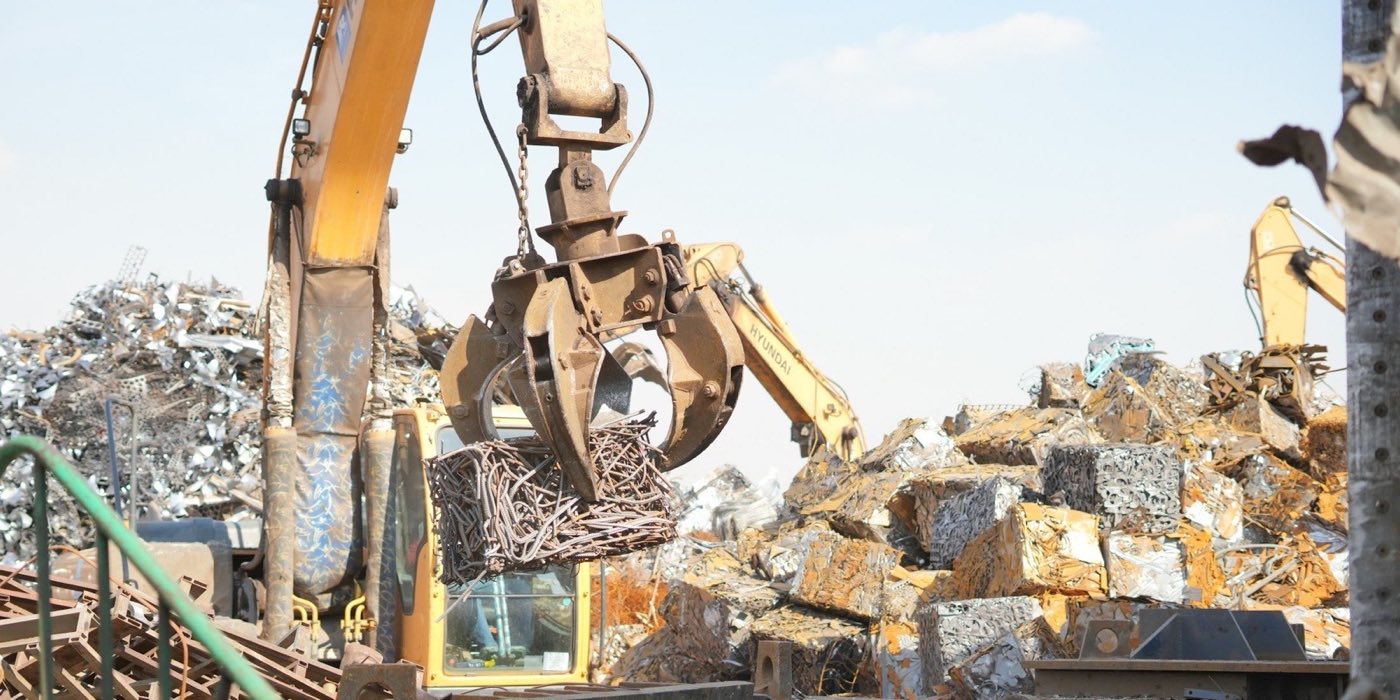 An excavator grab loading scrap in a yard